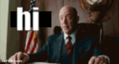 A Man In A Suit And Tie Is Sitting At A Desk In Front Of An American Flag With The Word Hi Above Him GIF