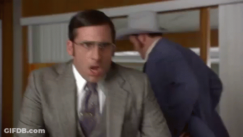 A Man In A Suit And Tie Is Sitting At A Desk While Another Man In A Cowboy Hat Looks On . GIF