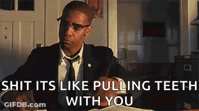 A Man In A Suit And Tie Is Sitting At A Desk With A Book And Glasses On . GIF