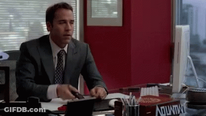 A Man In A Suit And Tie Is Sitting At A Desk With A Box On It That Says Aquafina GIF
