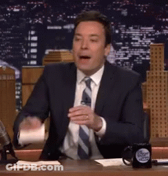 A Man In A Suit And Tie Is Sitting At A Desk With A Cup Of Coffee . GIF