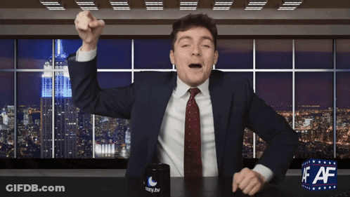 A Man In A Suit And Tie Is Sitting At A Desk With A Cup That Says Lazy.tv On It GIF