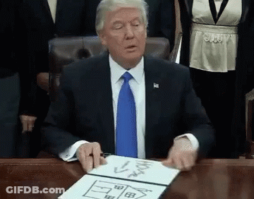 A Man In A Suit And Tie Is Sitting At A Desk With A Drawing Of A House On A Piece Of Paper . GIF