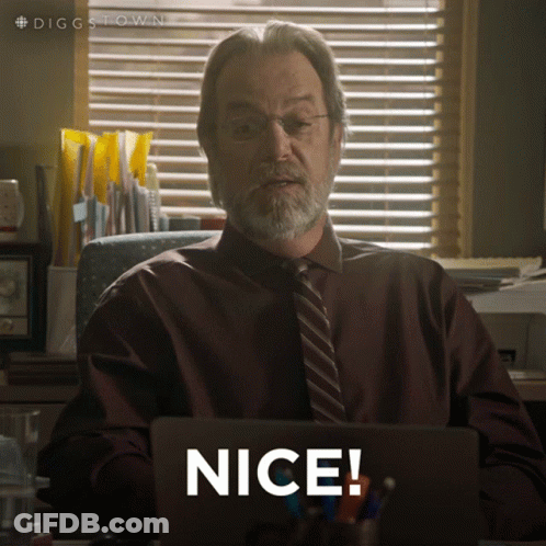 A Man In A Suit And Tie Is Sitting At A Desk With A Laptop And Says Nice GIF