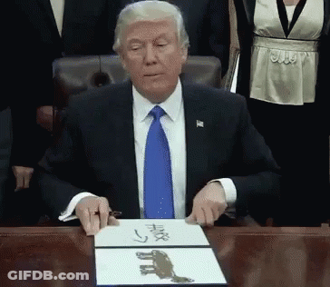 A Man In A Suit And Tie Is Sitting At A Desk With A Piece Of Paper That Says ' Trump ' On It GIF