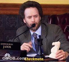 A Man In A Suit And Tie Is Sitting At A Desk With A Sign That Says Checkmate GIF