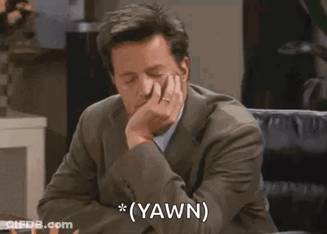A Man In A Suit And Tie Is Sitting At A Desk With His Hand On His Chin And Says `` Yawn '' . GIF
