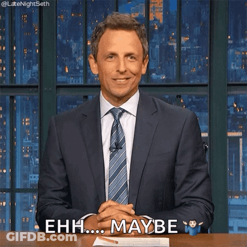A Man In A Suit And Tie Is Sitting At A Desk With His Hands Folded And Says Ehh Maybe GIF