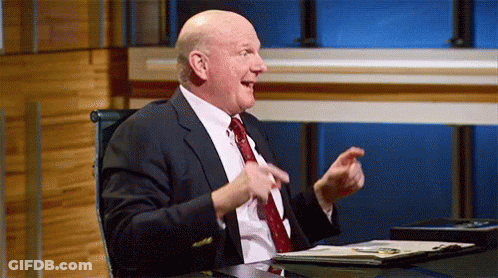 A Man In A Suit And Tie Is Sitting At A Desk With His Hands In The Air . GIF
