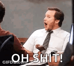 A Man In A Suit And Tie Is Sitting At A Desk With His Mouth Open And The Words `` Oh Shit ! '' GIF