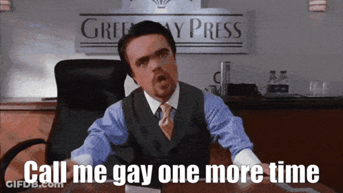 A Man In A Suit And Tie Is Sitting At A Desk With The Words Call Me Gay One More Time GIF