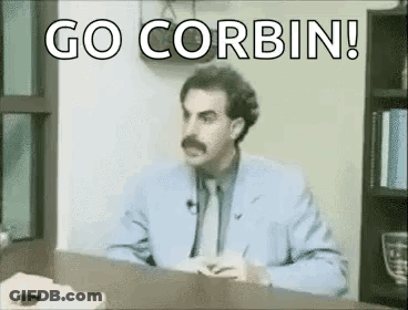 A Man In A Suit And Tie Is Sitting At A Desk With The Words `` Go Corbin '' Written On It . GIF