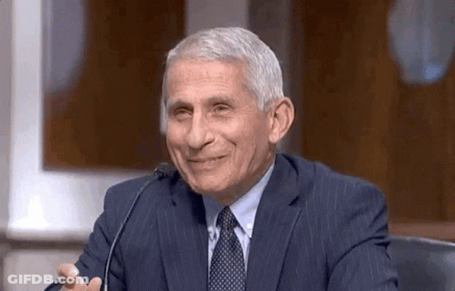 A Man In A Suit And Tie Is Sitting At A Microphone And Smiling . GIF