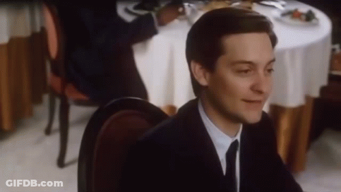 A Man In A Suit And Tie Is Sitting At A Restaurant Table . GIF
