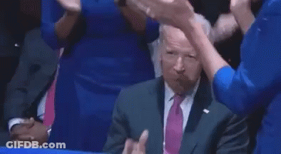A Man In A Suit And Tie Is Sitting At A Table And Pointing At Something . GIF