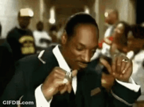 A Man In A Suit And Tie Is Sitting At A Table Eating A Sandwich . GIF