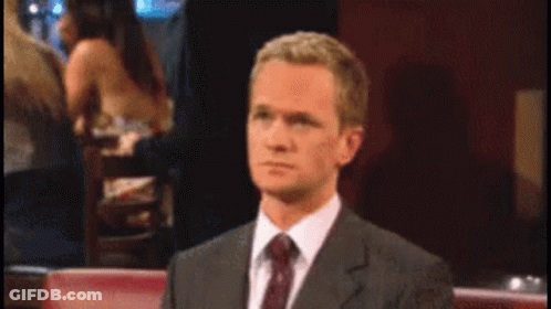 A Man In A Suit And Tie Is Sitting At A Table GIF