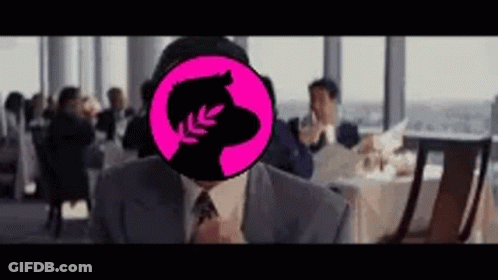 A Man In A Suit And Tie Is Sitting At A Table In A Restaurant With A Pink Circle On His Face . GIF