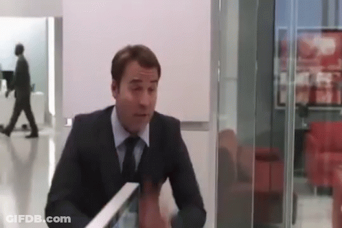 A Man In A Suit And Tie Is Sitting At A Table In A Room With A Glass Wall . GIF