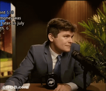 A Man In A Suit And Tie Is Sitting At A Table In Front Of A Microphone With A Mug That Says Af On It GIF