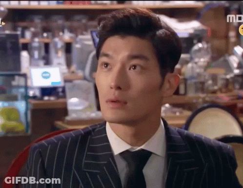 A Man In A Suit And Tie Is Sitting At A Table In Front Of A Sign That Says Md GIF