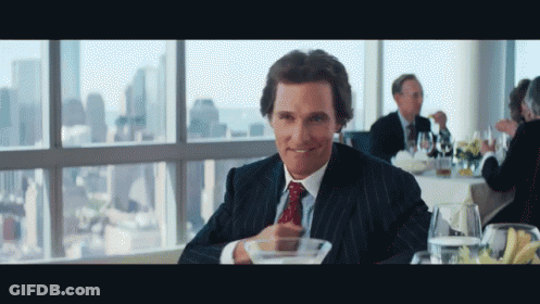 A Man In A Suit And Tie Is Sitting At A Table In Front Of A Window GIF