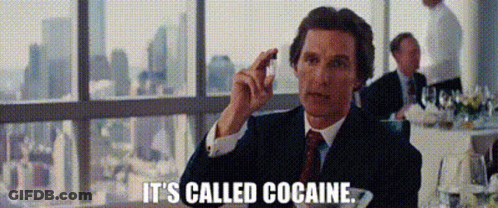 A Man In A Suit And Tie Is Sitting At A Table In Front Of A Window And Holding A Piece Of Chocolate . GIF