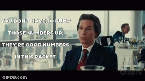 A Man In A Suit And Tie Is Sitting At A Table In Front Of A Window Talking To A Group Of People . GIF