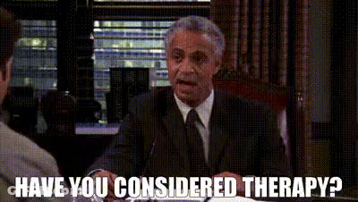 A Man In A Suit And Tie Is Sitting At A Table Talking To Another Man And Asking If He Considers Therapy . GIF