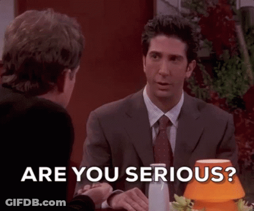 A Man In A Suit And Tie Is Sitting At A Table Talking To Another Man And Says Are You Serious . GIF