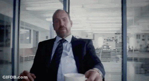 A Man In A Suit And Tie Is Sitting At A Table With A Cup Of Coffee . GIF