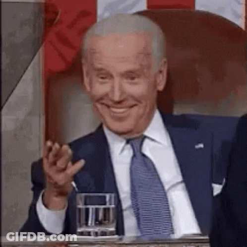 A Man In A Suit And Tie Is Sitting At A Table With A Glass Of Water And Smiling . GIF