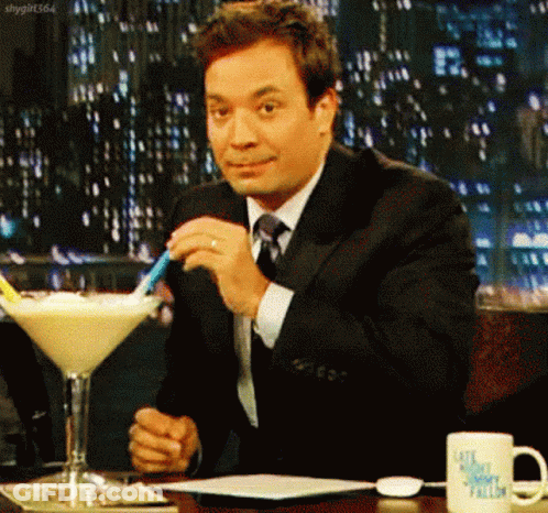 A Man In A Suit And Tie Is Sitting At A Table With A Martini Glass In Front Of Him GIF