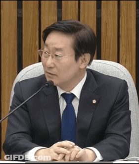 A Man In A Suit And Tie Is Sitting At A Table With A Microphone GIF