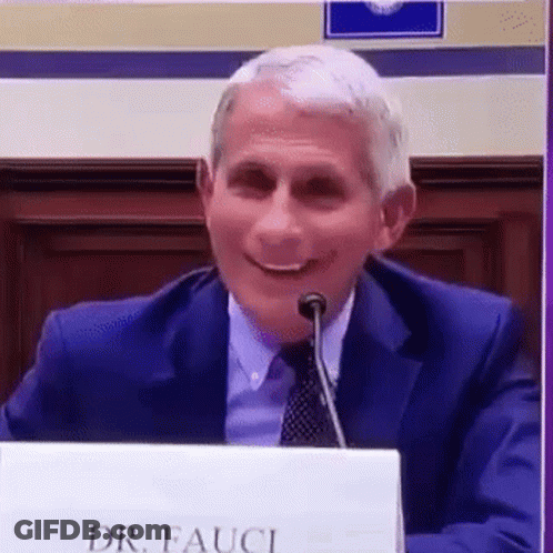 A Man In A Suit And Tie Is Sitting At A Table With A Microphone . GIF