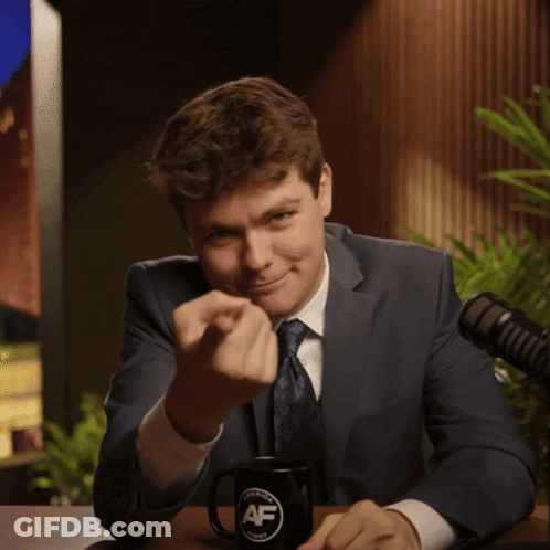 A Man In A Suit And Tie Is Sitting At A Table With A Mug That Says Af GIF