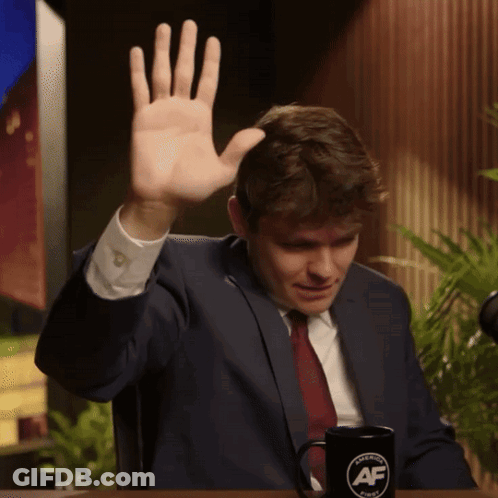 A Man In A Suit And Tie Is Sitting At A Table With A Mug That Says American Af GIF