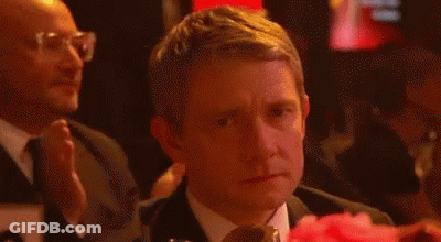 A Man In A Suit And Tie Is Sitting At A Table With A Pink Flower In Front Of Him . GIF