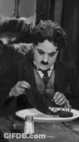 A Man In A Suit And Tie Is Sitting At A Table With A Plate Of Food And A Salt And Pepper Shaker GIF