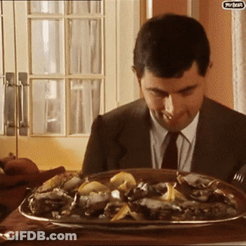 A Man In A Suit And Tie Is Sitting At A Table With A Plate Of Food In Front Of Him That Says Turkey On It GIF