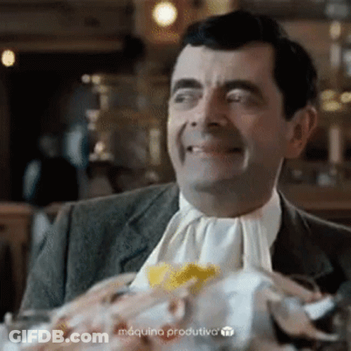 A Man In A Suit And Tie Is Sitting At A Table With A Plate Of Food On It . GIF