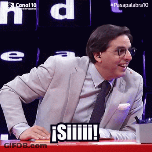 A Man In A Suit And Tie Is Sitting At A Table With A Sign That Says ' Siiiiii ' On It GIF