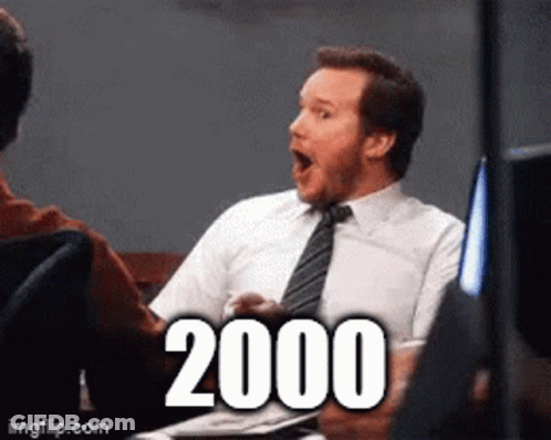A Man In A Suit And Tie Is Sitting At A Table With A Surprised Look On His Face And The Number 2000 Written On The Scree GIF