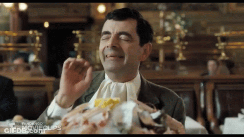 A Man In A Suit And Tie Is Sitting At A Table With His Eyes Closed And A Pile Of Food .. GIF