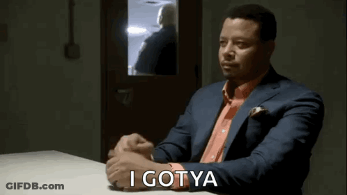 A Man In A Suit And Tie Is Sitting At A Table With His Hands Folded And Says `` I Gotya '' . GIF