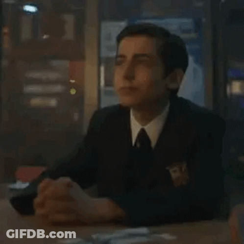 A Man In A Suit And Tie Is Sitting At A Table With His Hands Folded In Prayer . GIF