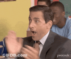 A Man In A Suit And Tie Is Sitting At A Table With His Hands In The Air And His Mouth Open . GIF