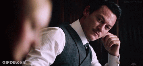 A Man In A Suit And Tie Is Sitting At A Table With His Hands On His Chin . GIF