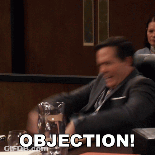 A Man In A Suit And Tie Is Sitting At A Table With Objection Written On It GIF