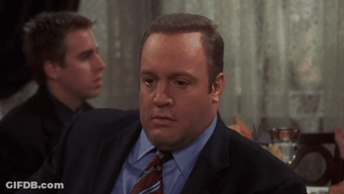 A Man In A Suit And Tie Is Sitting At A Table With Other Men GIF